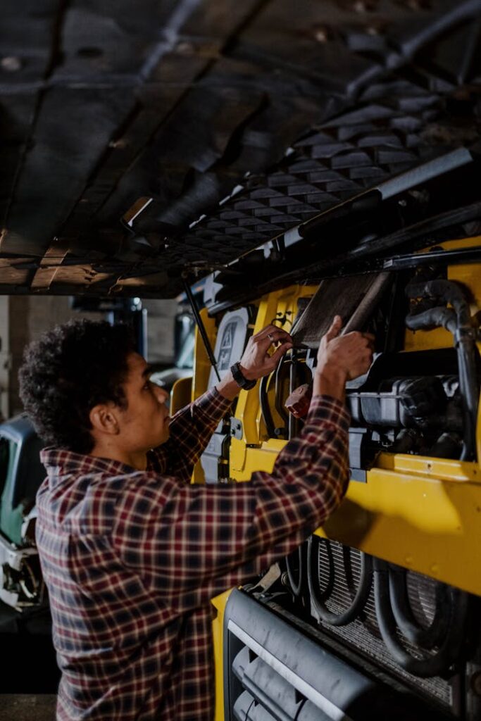 Auto mechanic working on a vehicle engine in an indoor garage setting, focused on mechanical repair.