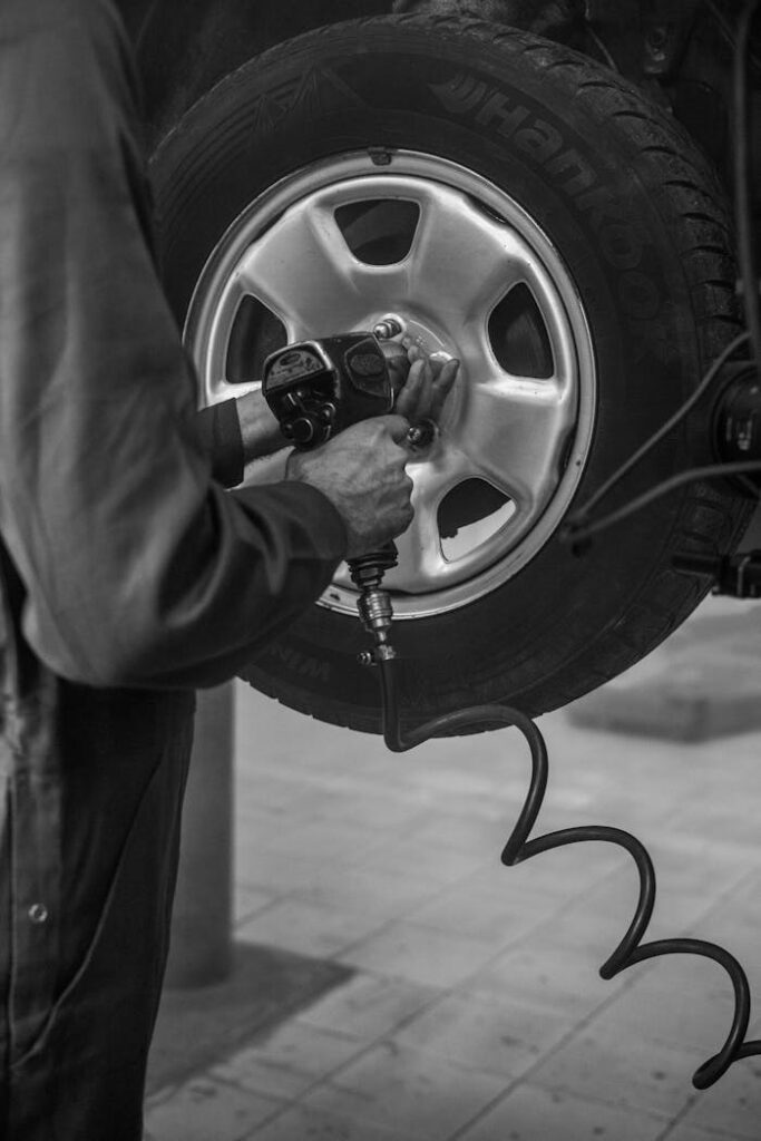 Mechanic uses air wrench to fix car tire in a monochrome garage setting.